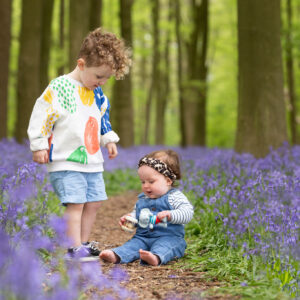 Two siblings sit on a path between a carpet of bluebells during an Ashridge Estate Bluebell photoshoot