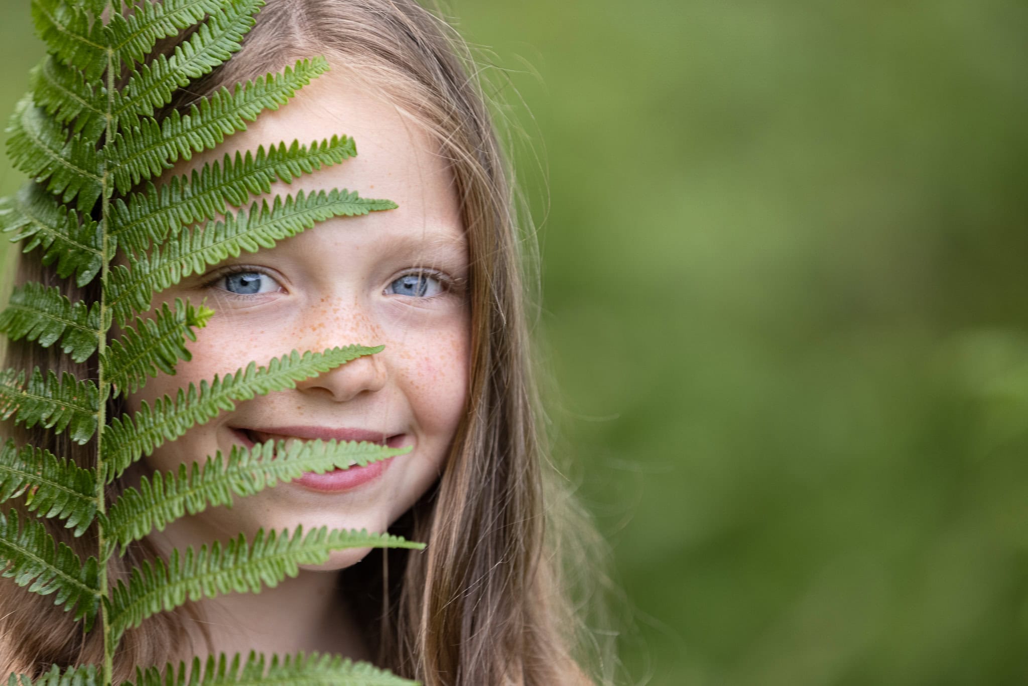Girl holding a fern leave smiles at camera during photoshoot