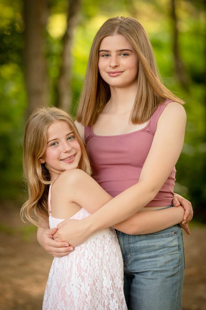 Two teenage sisters embrace during an outdoor photoshoot, in beautiful golden evening light