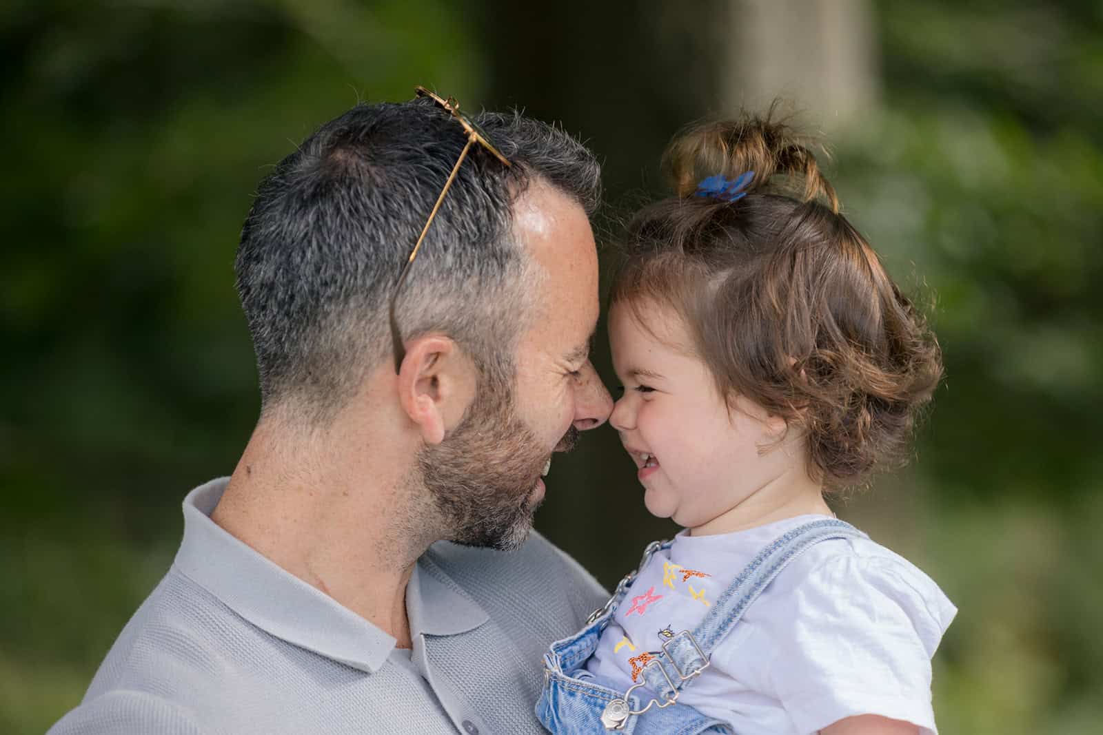 A dad and daughter do an eskimo kiss, surrounded by beautiful trees
