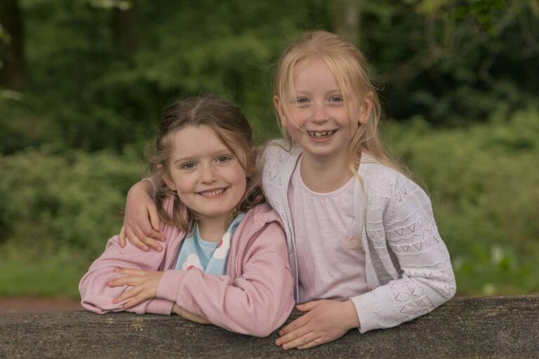 Cousins smile at the camera while climbing a gate during an extended family photoshoot