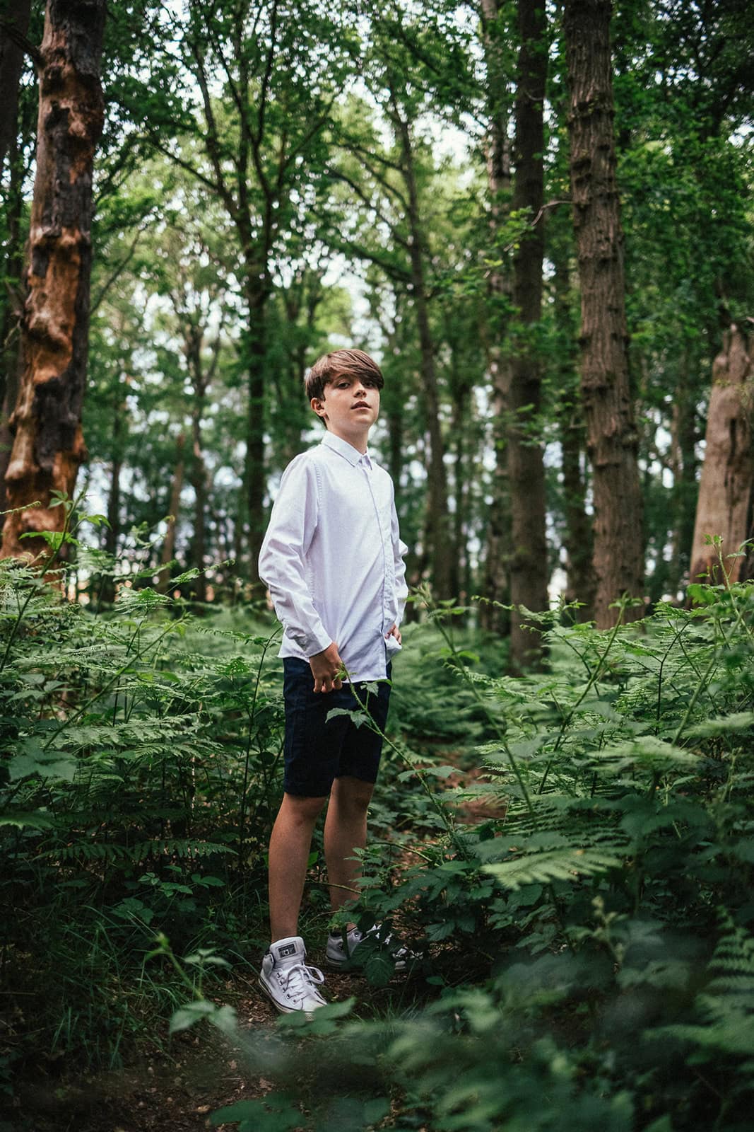 A teen stands tall among tall trees, the photo is shot from a low angle
