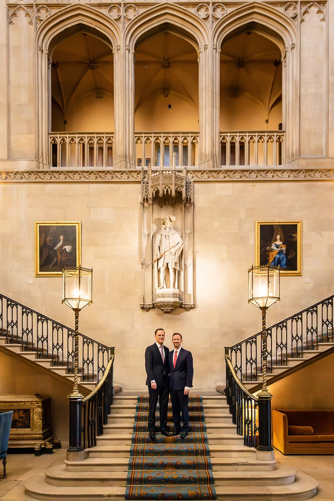 Two grooms pose for photos on the internatl staircase at Ashridge House