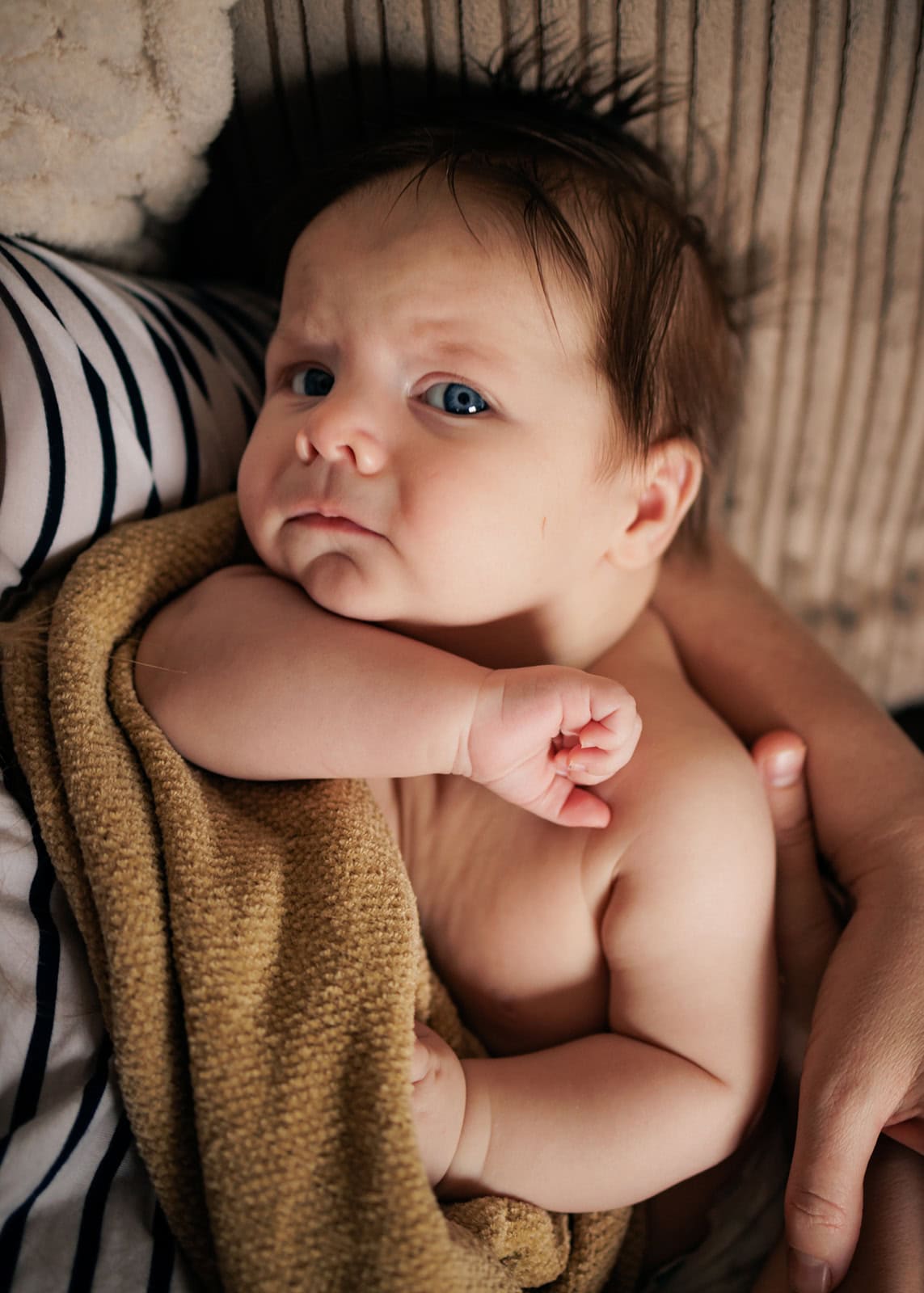 Older baby looks directly into the camera from where he is resting in his mum's arms in Berkhamsted