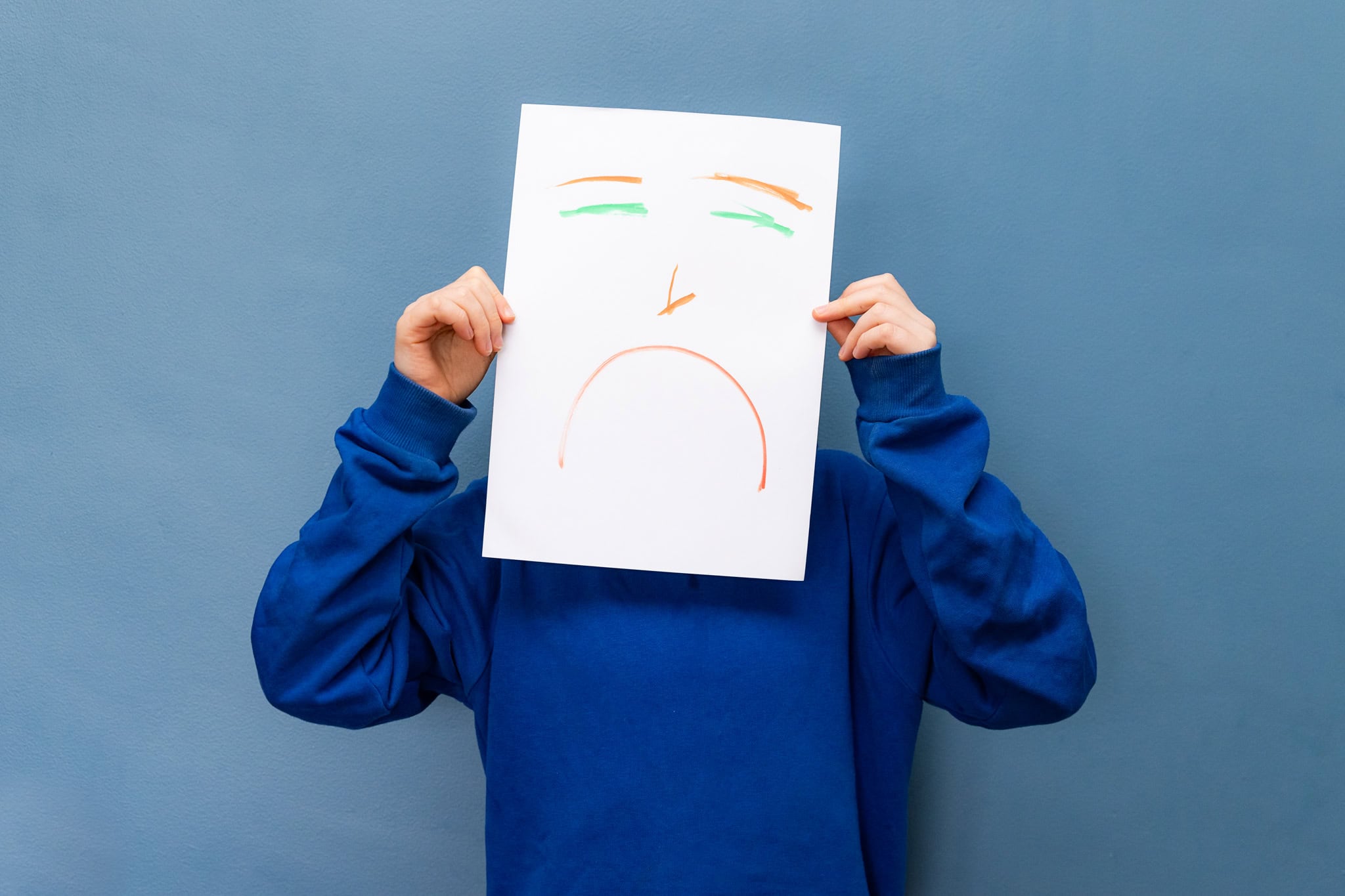 Child holds a pieve of paper with a sad expression in front of their own face