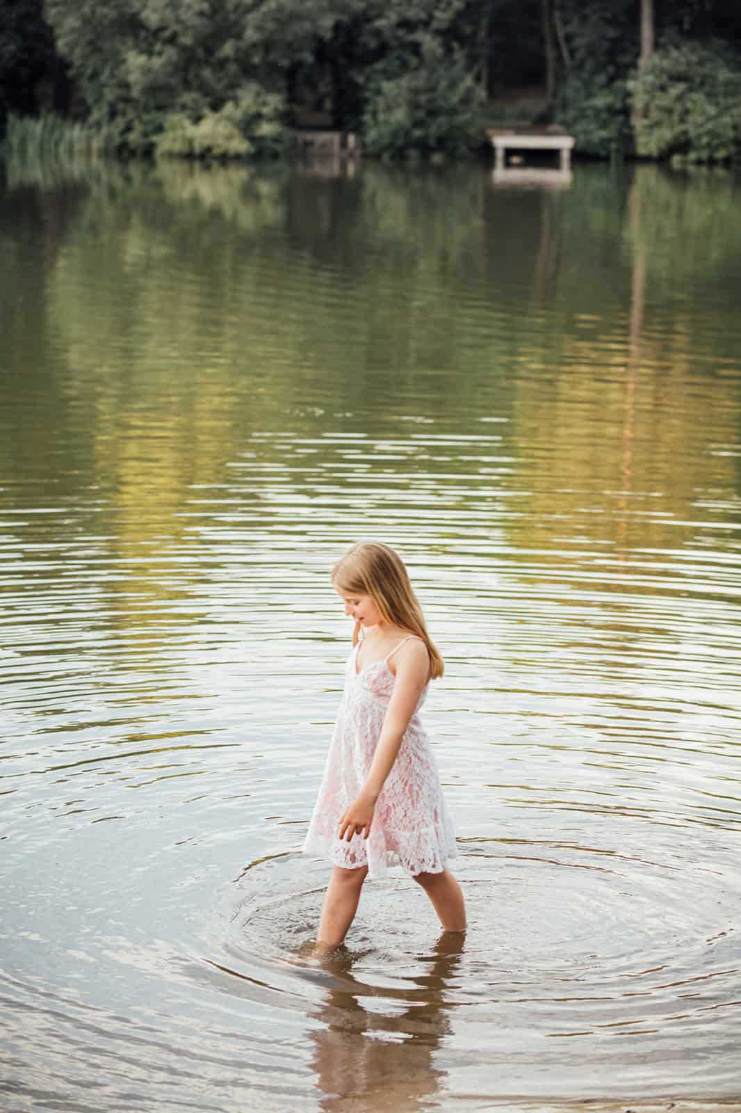 A girl paddles in the edge of a lake on London at golden hour during a family photoshoot
