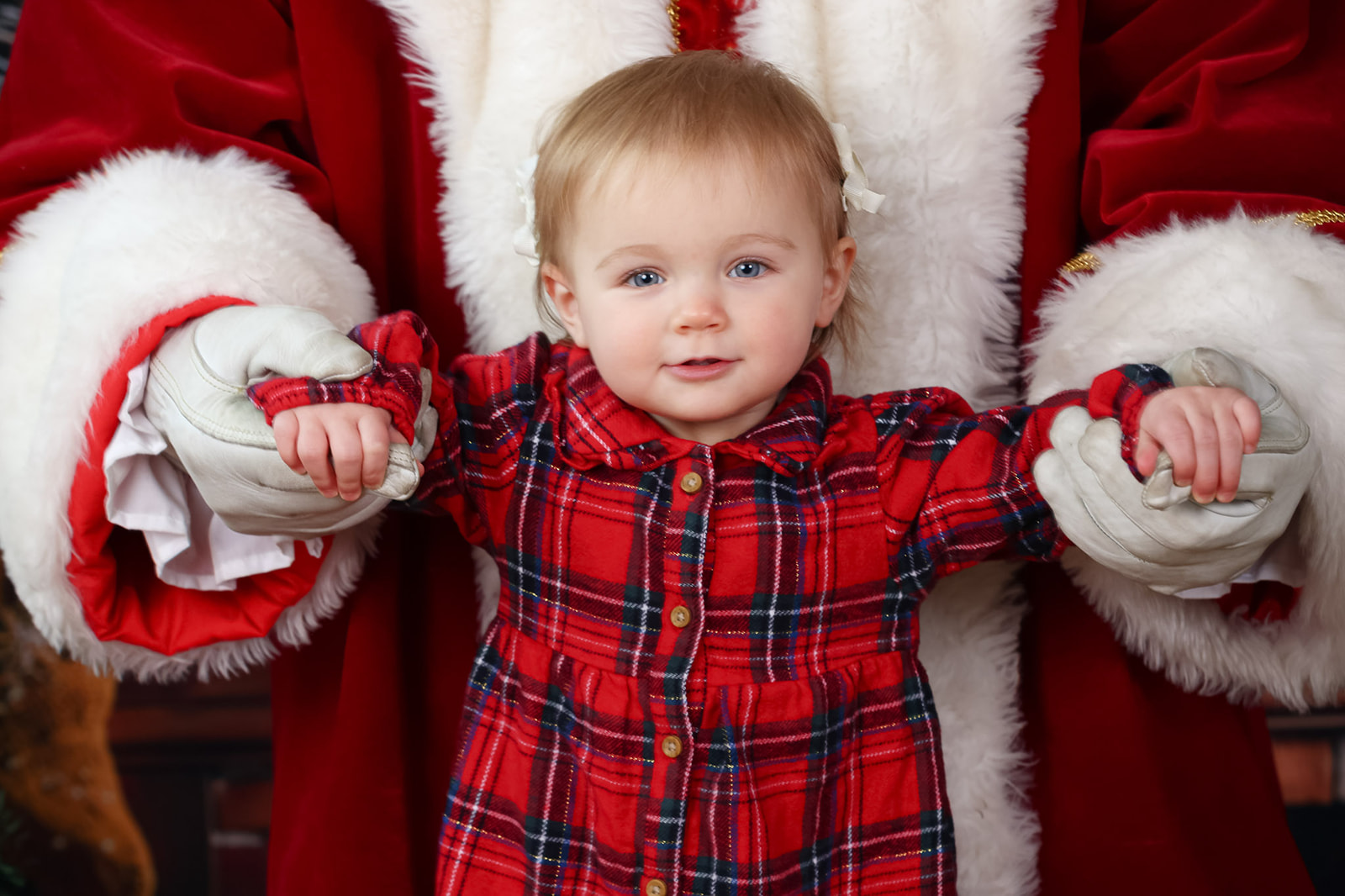 A baby stands with santa supporting both her arms during a Santa photoshoot near St Albans