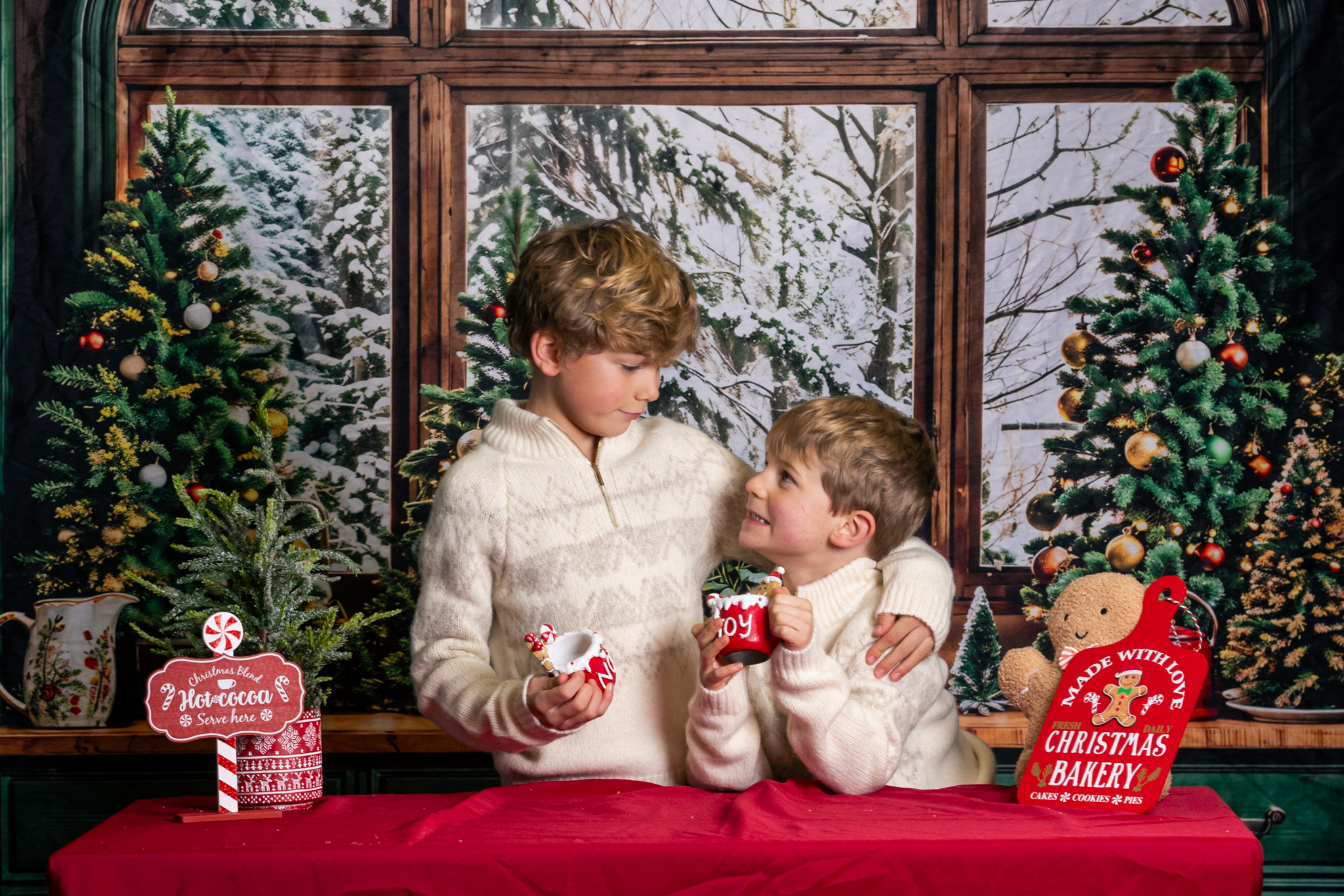 Two brothers smile at each other while pretending to drink hot chocolate and roll dough for gingerbread men. She's having a Christmas photoshoot near St Albans.